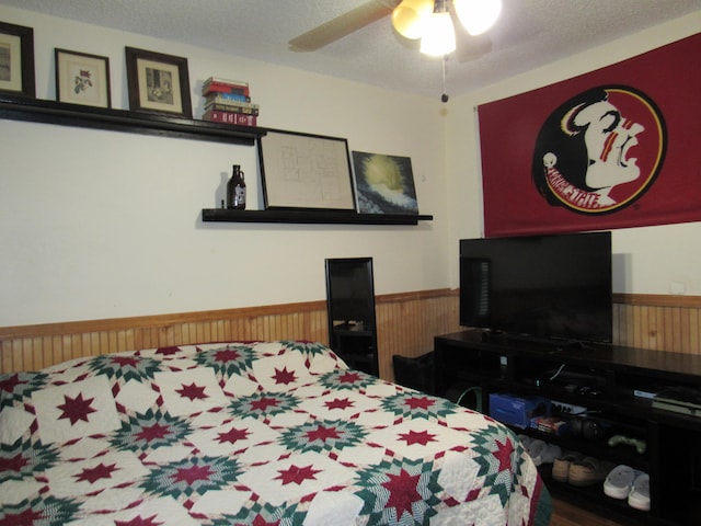 bedroom with wood walls, a textured ceiling, and ceiling fan