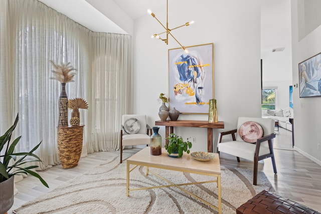 living area with light hardwood / wood-style floors, an inviting chandelier, and a high ceiling