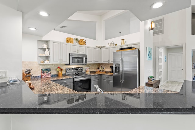 kitchen featuring appliances with stainless steel finishes, kitchen peninsula, dark stone counters, and backsplash