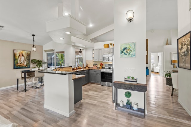 kitchen featuring appliances with stainless steel finishes, kitchen peninsula, light hardwood / wood-style floors, vaulted ceiling, and gray cabinets