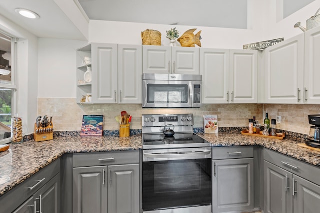 kitchen with gray cabinets, appliances with stainless steel finishes, dark stone countertops, and tasteful backsplash