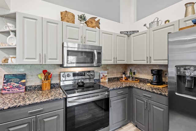 kitchen featuring gray cabinets, tasteful backsplash, stainless steel appliances, and dark stone counters