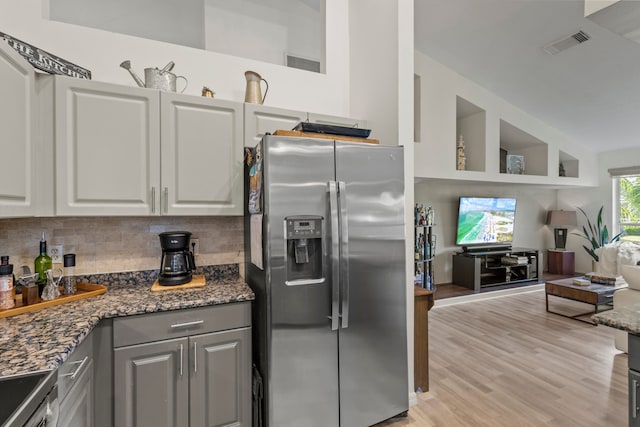 kitchen featuring decorative backsplash, light hardwood / wood-style flooring, dark stone countertops, gray cabinets, and stainless steel appliances