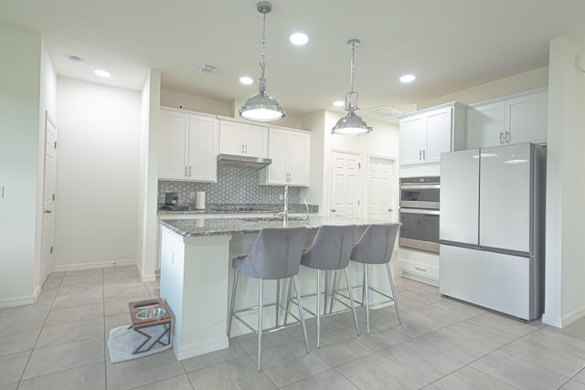 kitchen with double oven, white cabinets, white fridge, and an island with sink