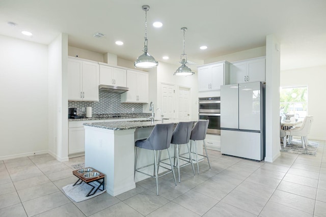 kitchen featuring white cabinetry, sink, white fridge, dark stone counters, and a kitchen island with sink