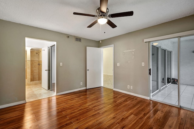 unfurnished bedroom with ceiling fan, a textured ceiling, ensuite bathroom, and light wood-type flooring