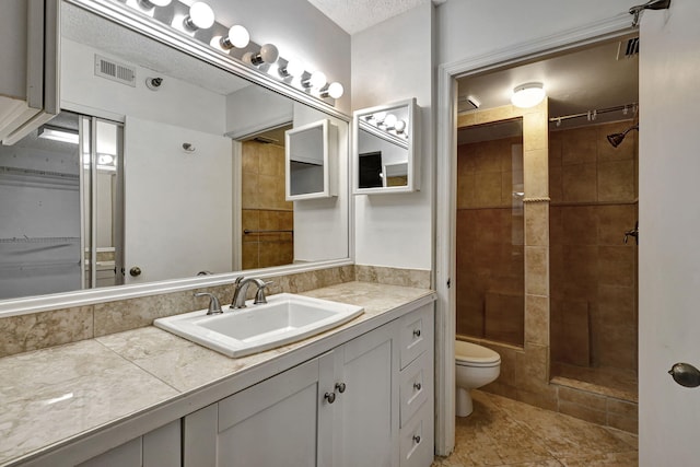 bathroom featuring tile patterned floors, toilet, vanity, a tile shower, and a textured ceiling