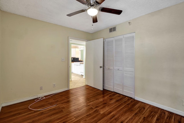 unfurnished bedroom featuring dark wood-type flooring, a textured ceiling, a closet, and ceiling fan