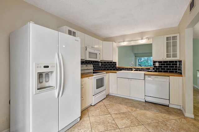 kitchen featuring white appliances, a textured ceiling, white cabinetry, and light tile patterned flooring