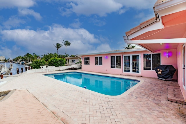 view of swimming pool featuring a grill, a water view, and a patio