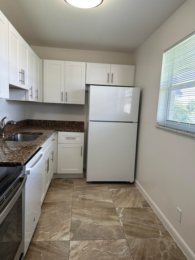 kitchen with dishwasher, dark stone countertops, sink, white refrigerator, and white cabinets