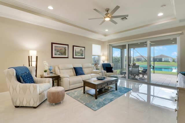 living room with crown molding, a water view, a tray ceiling, and ceiling fan