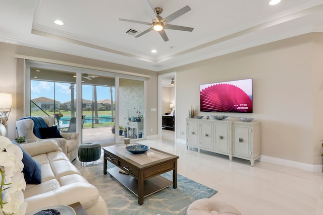 living room with ceiling fan, a raised ceiling, ornamental molding, and light tile patterned floors