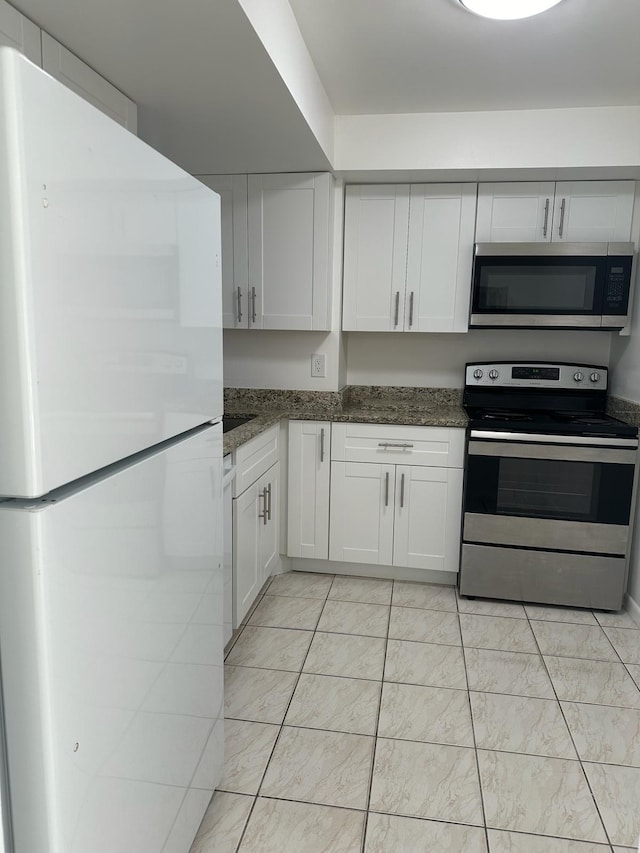 kitchen featuring white cabinetry, dark stone countertops, appliances with stainless steel finishes, and light tile patterned flooring