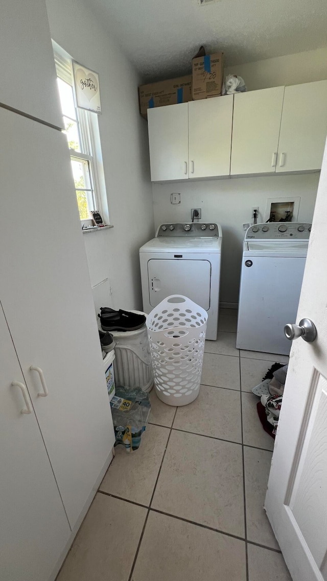 clothes washing area with cabinets, light tile patterned floors, and washer and clothes dryer