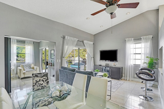 tiled dining space featuring a textured ceiling, a healthy amount of sunlight, high vaulted ceiling, and ceiling fan