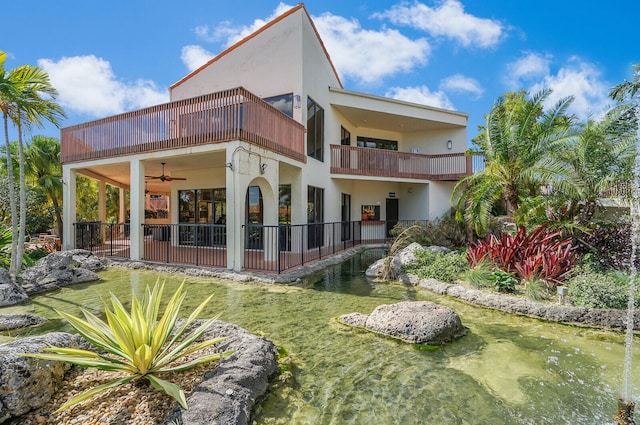 rear view of property with a balcony, a water view, a lawn, and ceiling fan