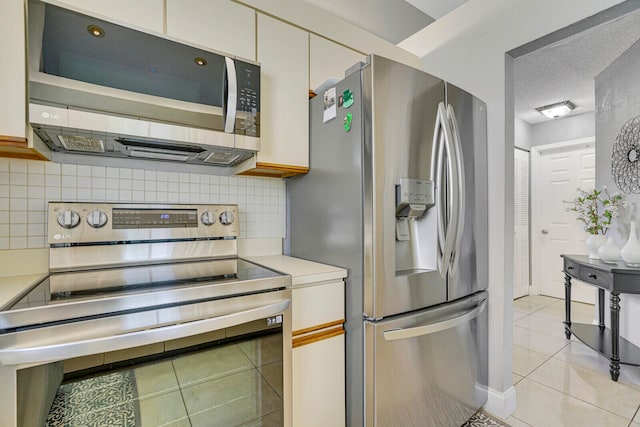 kitchen featuring appliances with stainless steel finishes, decorative backsplash, light tile patterned flooring, and a textured ceiling