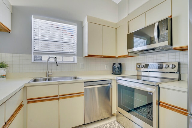 kitchen featuring appliances with stainless steel finishes, light tile patterned flooring, sink, cream cabinets, and backsplash