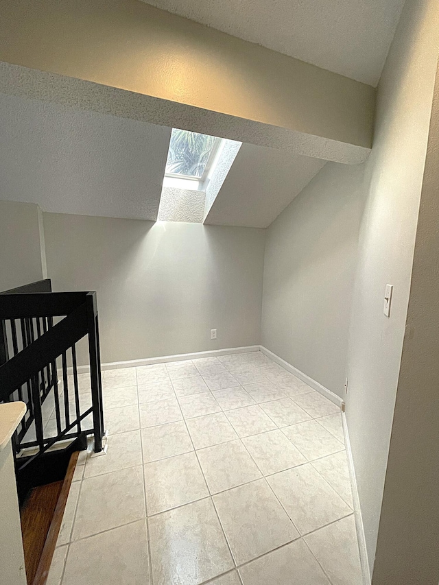 additional living space featuring lofted ceiling with skylight and light tile patterned flooring