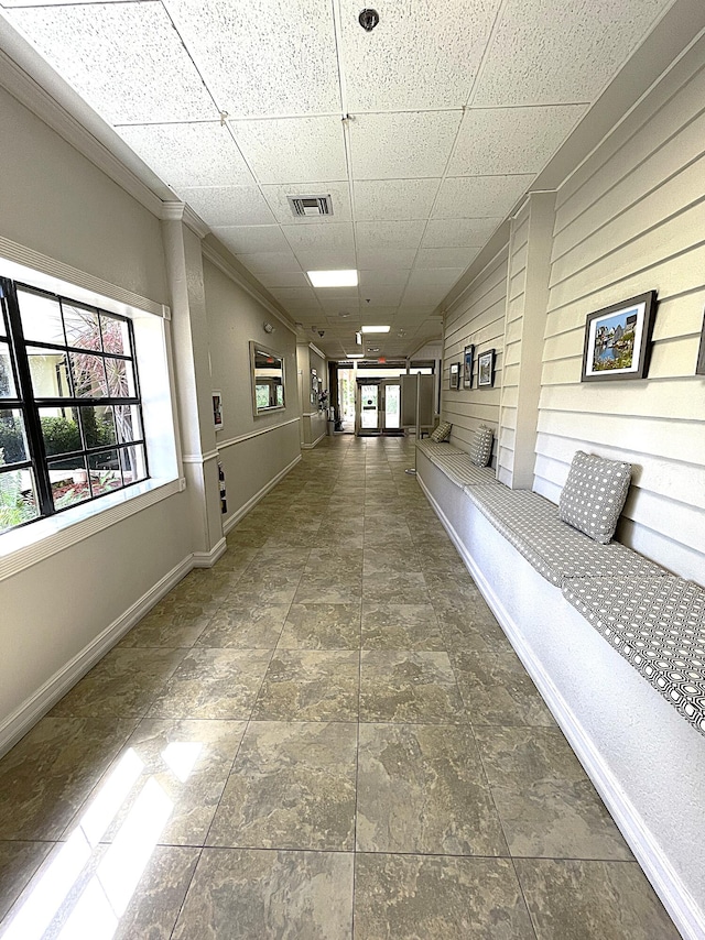 corridor featuring wood walls, a paneled ceiling, a healthy amount of sunlight, and crown molding