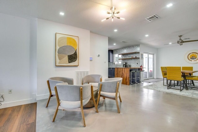 dining space with ceiling fan with notable chandelier, bar, a textured ceiling, and light hardwood / wood-style flooring