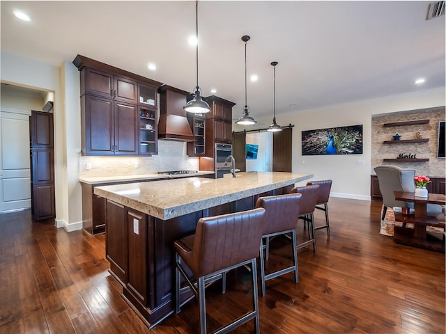 kitchen featuring a kitchen bar, decorative light fixtures, custom exhaust hood, dark wood-type flooring, and a kitchen island with sink