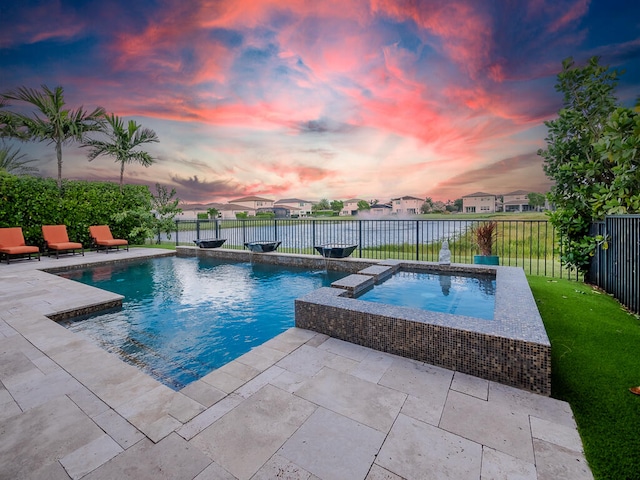 pool at dusk with an in ground hot tub, a patio area, a water view, and a yard