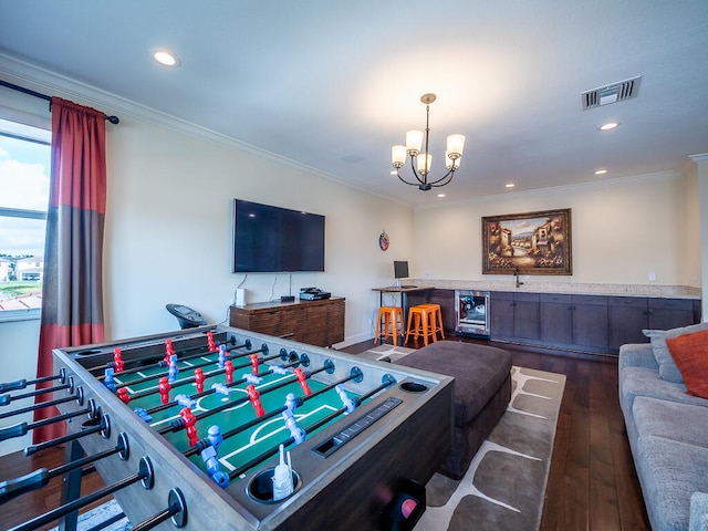 recreation room with wine cooler, dark wood-type flooring, crown molding, and an inviting chandelier