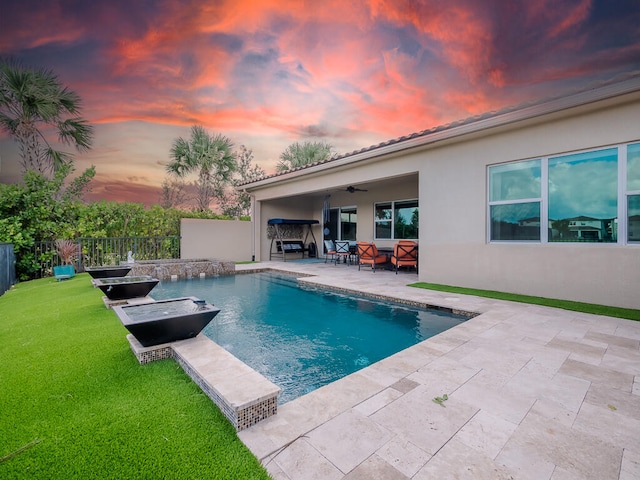 pool at dusk with a yard, a patio area, and ceiling fan