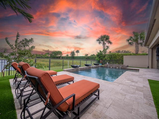 pool at dusk featuring a patio and pool water feature