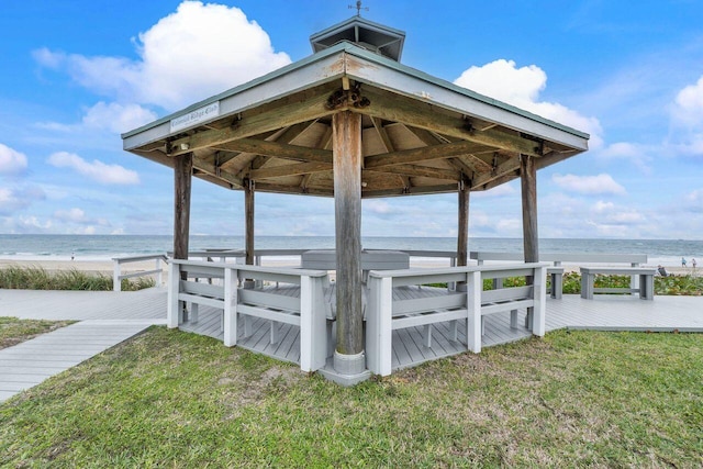 view of dock with a gazebo, a deck with water view, a lawn, and a view of the beach