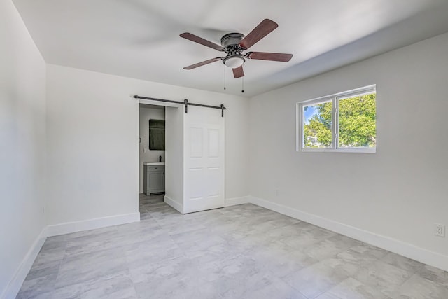 unfurnished bedroom with ceiling fan, a barn door, and ensuite bath