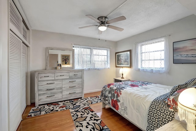 bedroom featuring light hardwood / wood-style flooring, a textured ceiling, a closet, and ceiling fan