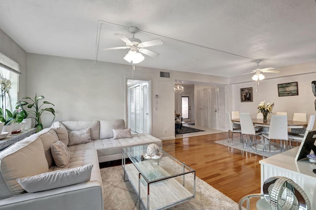 living room with ceiling fan, a textured ceiling, and light wood-type flooring