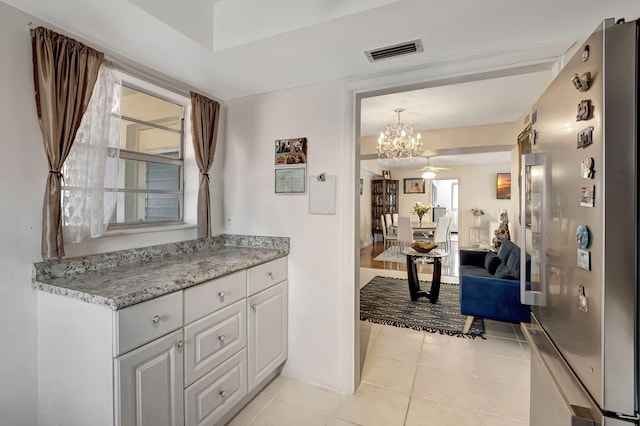 interior space with ceiling fan with notable chandelier, stainless steel fridge, pendant lighting, white cabinets, and light tile patterned floors