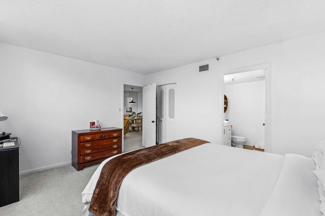 bedroom featuring a closet, ensuite bath, a textured ceiling, and light colored carpet