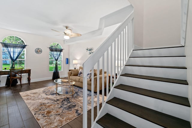 living room featuring dark wood-style floors, a ceiling fan, baseboards, and stairs