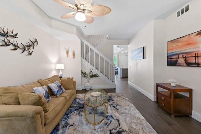 living area featuring baseboards, visible vents, dark wood finished floors, a ceiling fan, and stairway