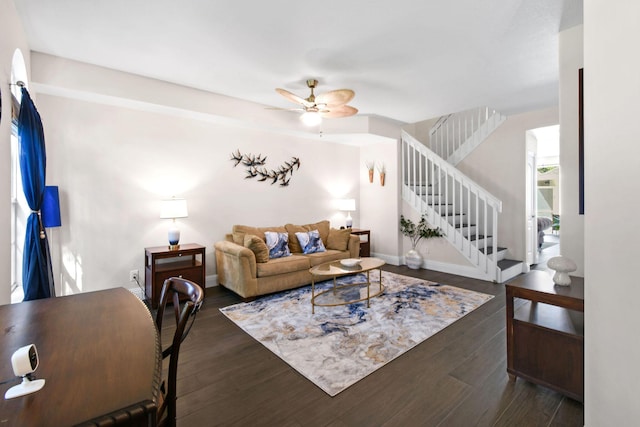 living area with a ceiling fan, dark wood finished floors, baseboards, and stairs