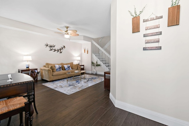 living room featuring stairs, ceiling fan, dark wood-type flooring, and baseboards