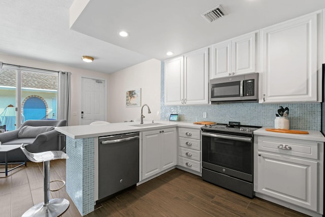 kitchen with a peninsula, white cabinetry, stainless steel appliances, and a sink