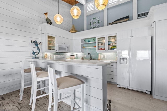 kitchen featuring pendant lighting, white cabinetry, a towering ceiling, white appliances, and a breakfast bar