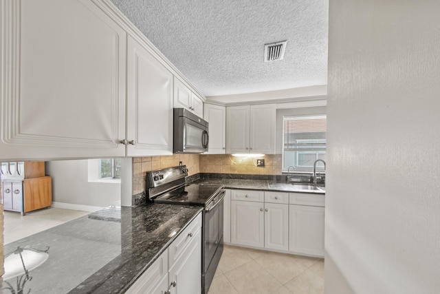 kitchen featuring white cabinets, light tile patterned floors, stainless steel electric range oven, and dark stone counters