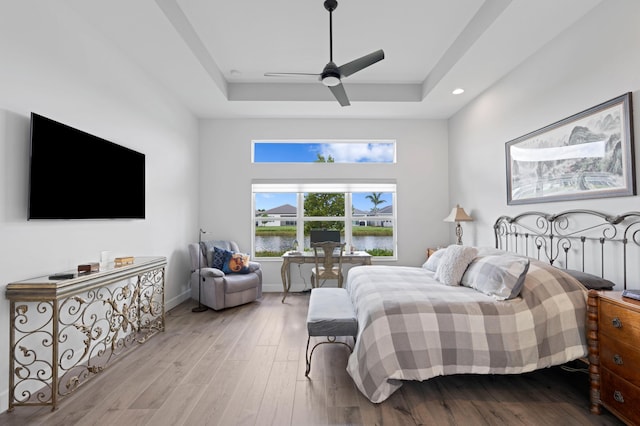 bedroom featuring light hardwood / wood-style floors, a raised ceiling, ceiling fan, and a water view