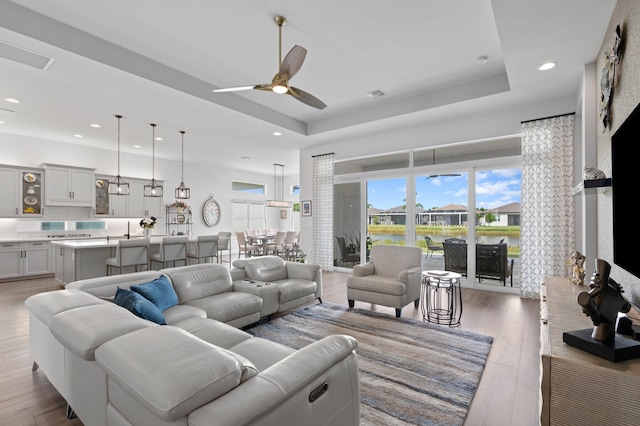 living room with hardwood / wood-style flooring, ceiling fan, and a tray ceiling