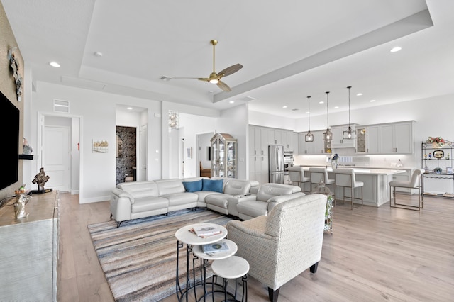 living room with light wood-type flooring, a tray ceiling, and ceiling fan