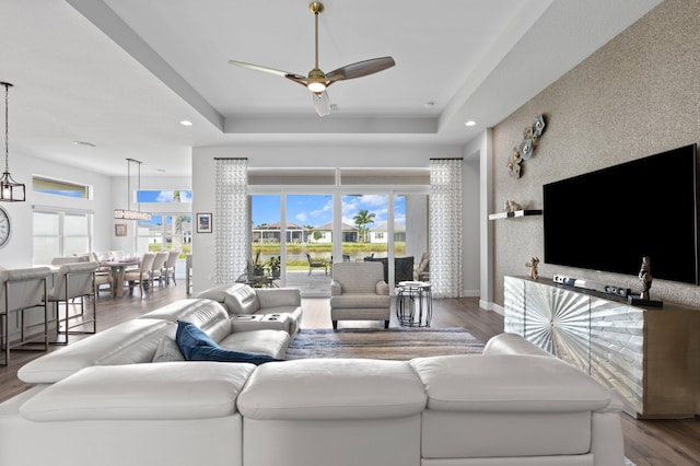 living room with hardwood / wood-style flooring, ceiling fan, and a tray ceiling