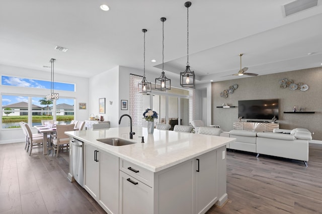 kitchen with a kitchen island with sink, sink, ceiling fan, light stone counters, and white cabinetry