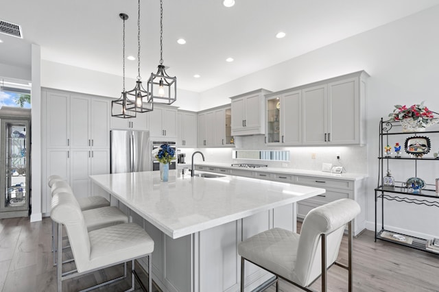 kitchen featuring sink, stainless steel appliances, an island with sink, a breakfast bar, and light wood-type flooring